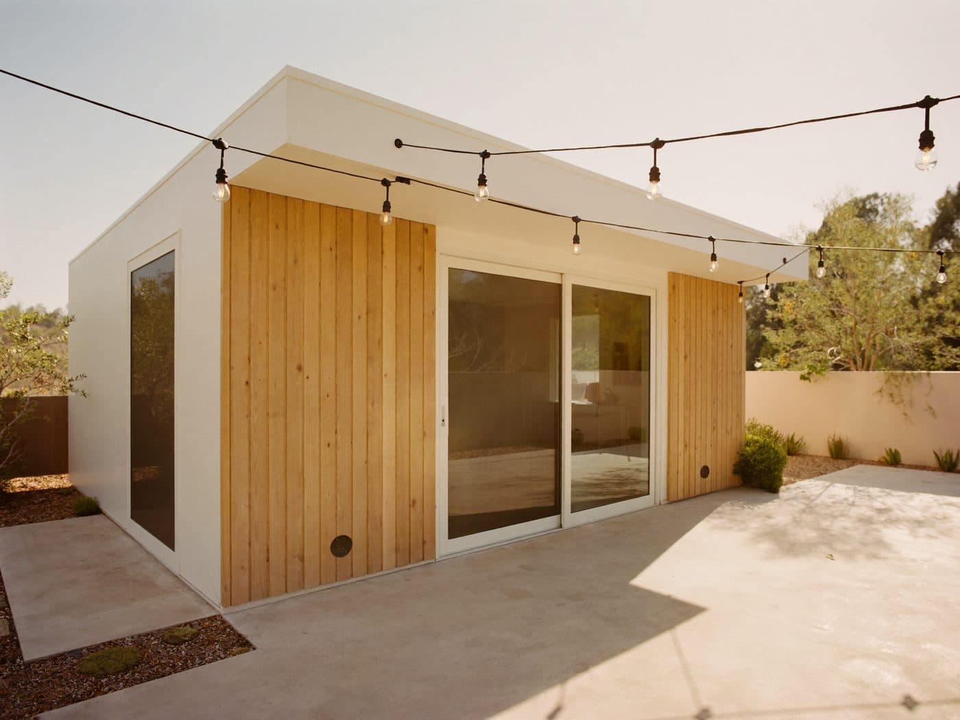 Detached backyard ADU with wood siding, sliding glass doors and string lights