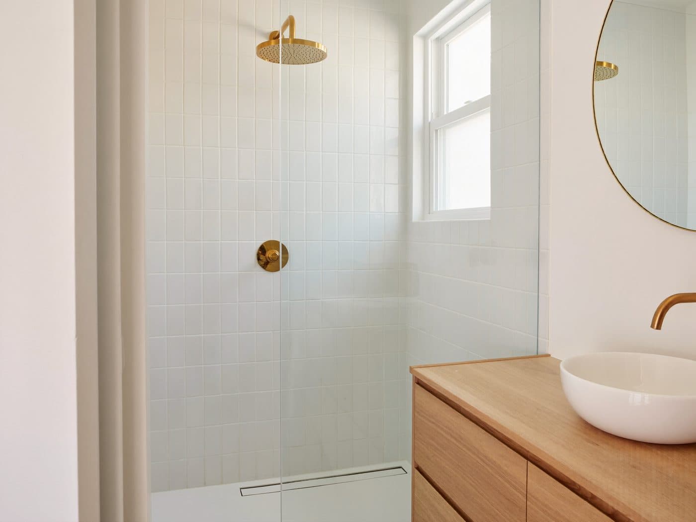 Modern bathroom with a white tiled shower, brass fixtures and an oak vanity